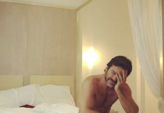 Paolo Conticini a piedi nudi e senza maglietta a letto appena sveglio
