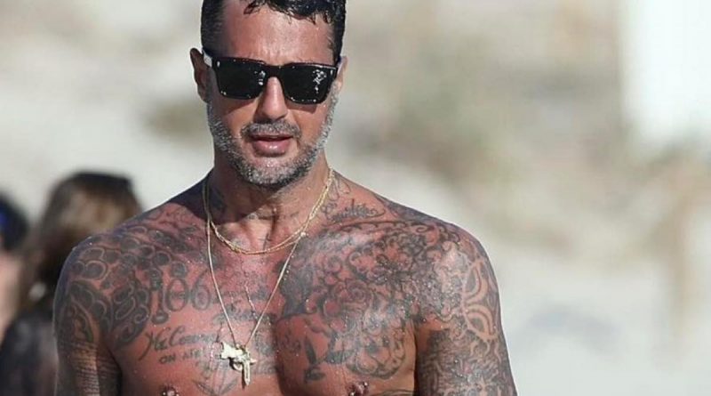 Fabrizio Corona cammina in spiaggia e le mani che si appoggiano proprio li